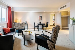 Een moderne hotelkamer met een zithoek, eettafel en uitzicht op de stad.