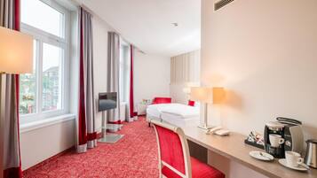 Habitación de hotel con cama, escritorio con teléfono y cafetera, una silla y televisor montado en la pared.
