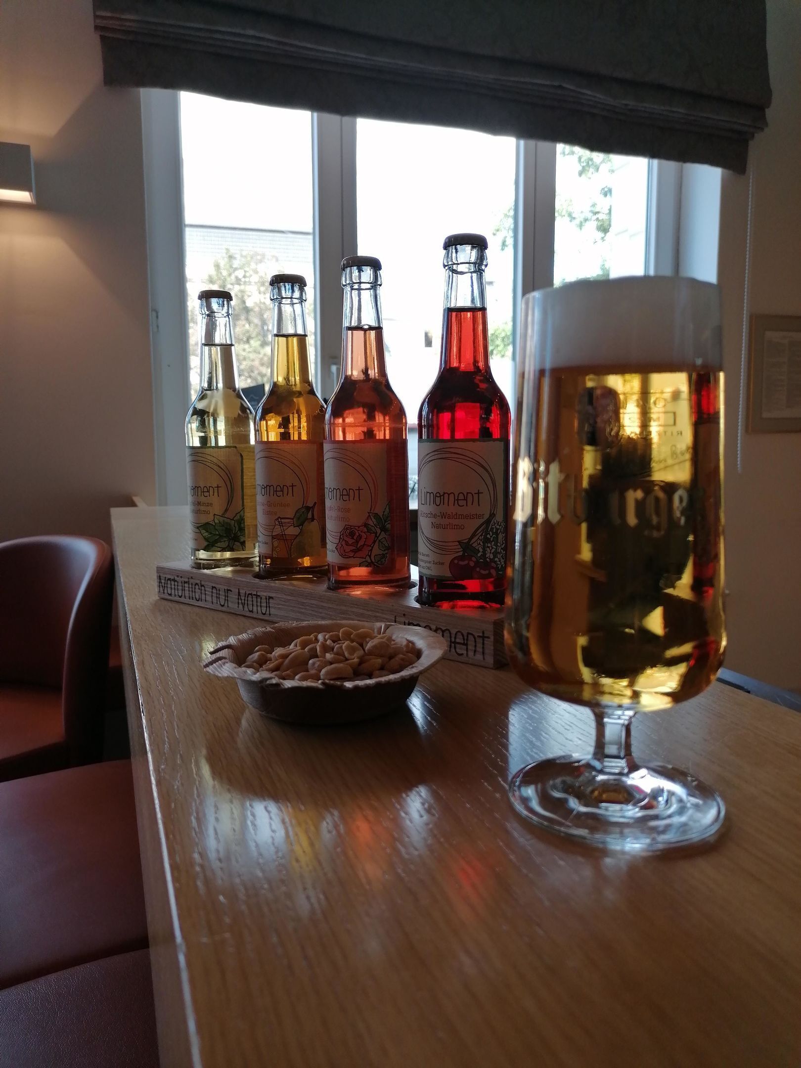 A table with four bottles of beer and a glass of beer, a bowl of nuts, and a sign with the word "Naturlich".