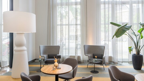 Un hall d’hôtel moderne avec une table ronde, deux fauteuils, un lampadaire et une grande plante en pot.