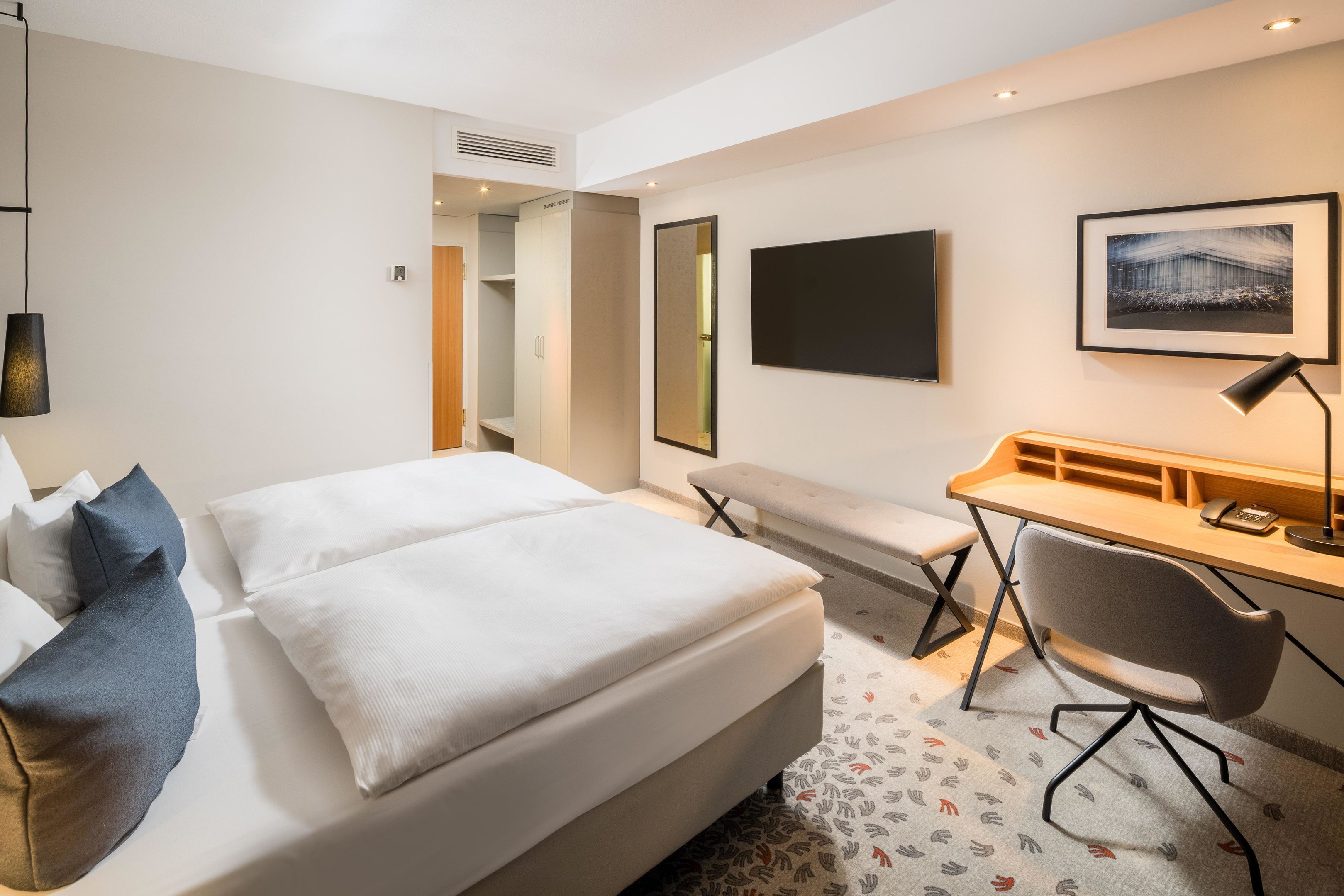 A hotel room with a bed, a desk, a chair, a TV, and a mirror.