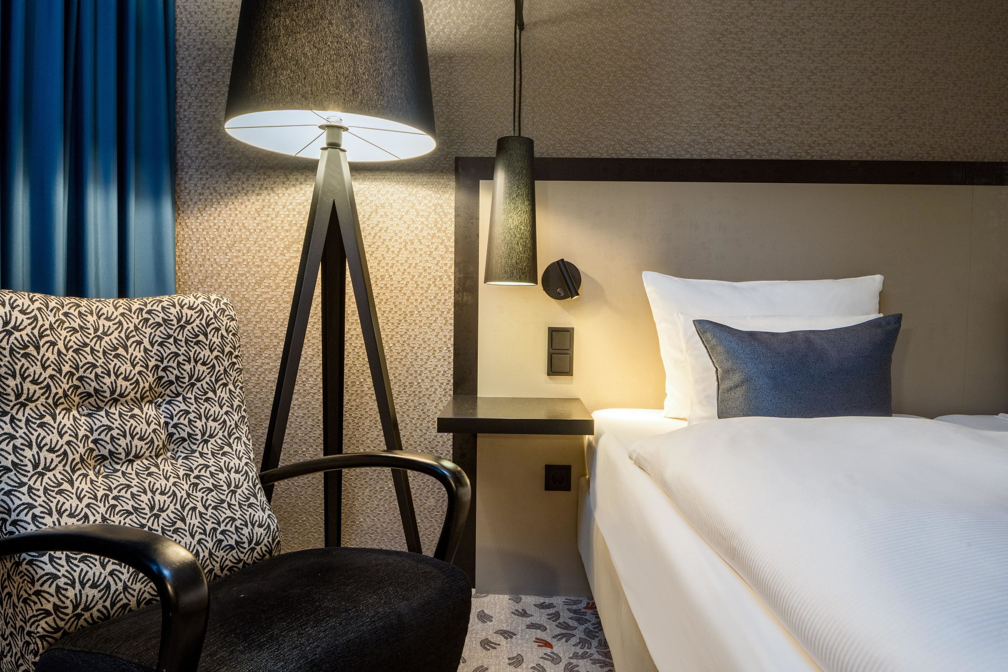 Habitación de hotel con una cama, una silla, un escritorio, una lámpara y un reloj de pared.