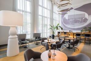 A modern hotel lobby with a large white lamp, comfortable seating, a large window, and a projection screen.