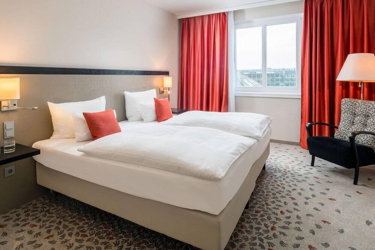 Een hotelkamer met een groot bed, rode gordijnen, een kamerbreed tapijt en een stoel.