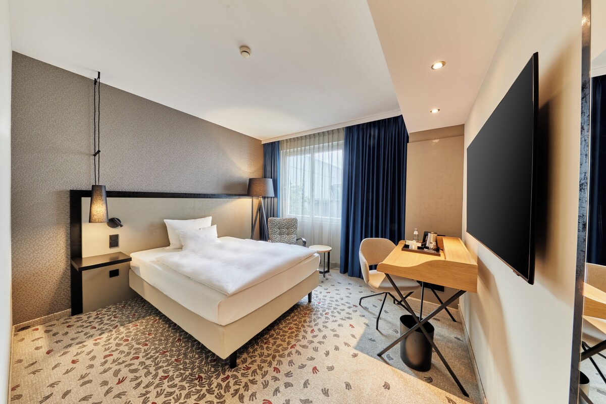 Habitación de hotel con cama, escritorio, silla, televisor y alfombra estampada.