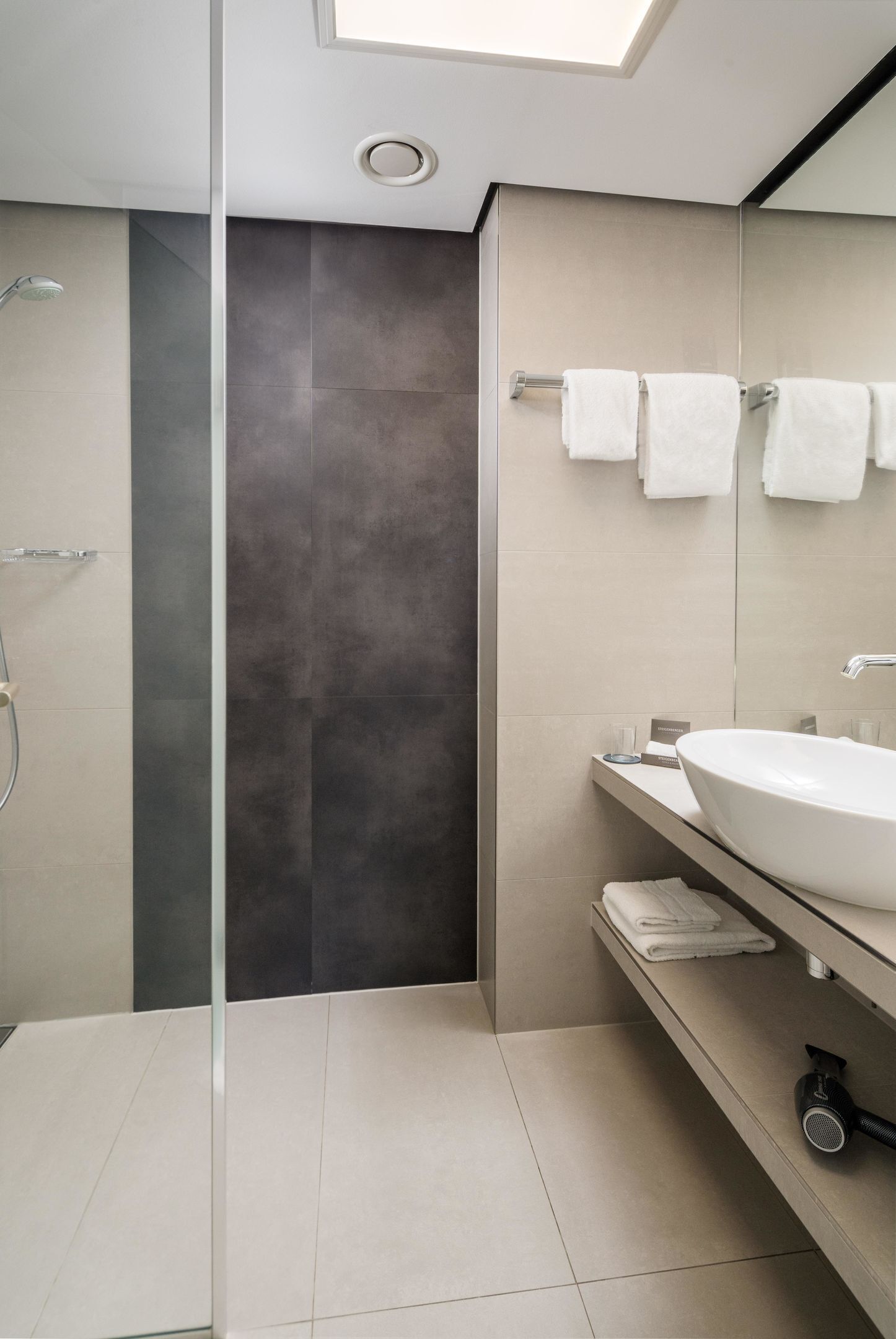 A modern bathroom with a skylight, a large mirror, a sink, and a shower.
