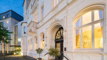 Un edificio histórico con arquitectura ornamentada, una entrada destacada y un interior bien iluminado visible a través de las ventanas.