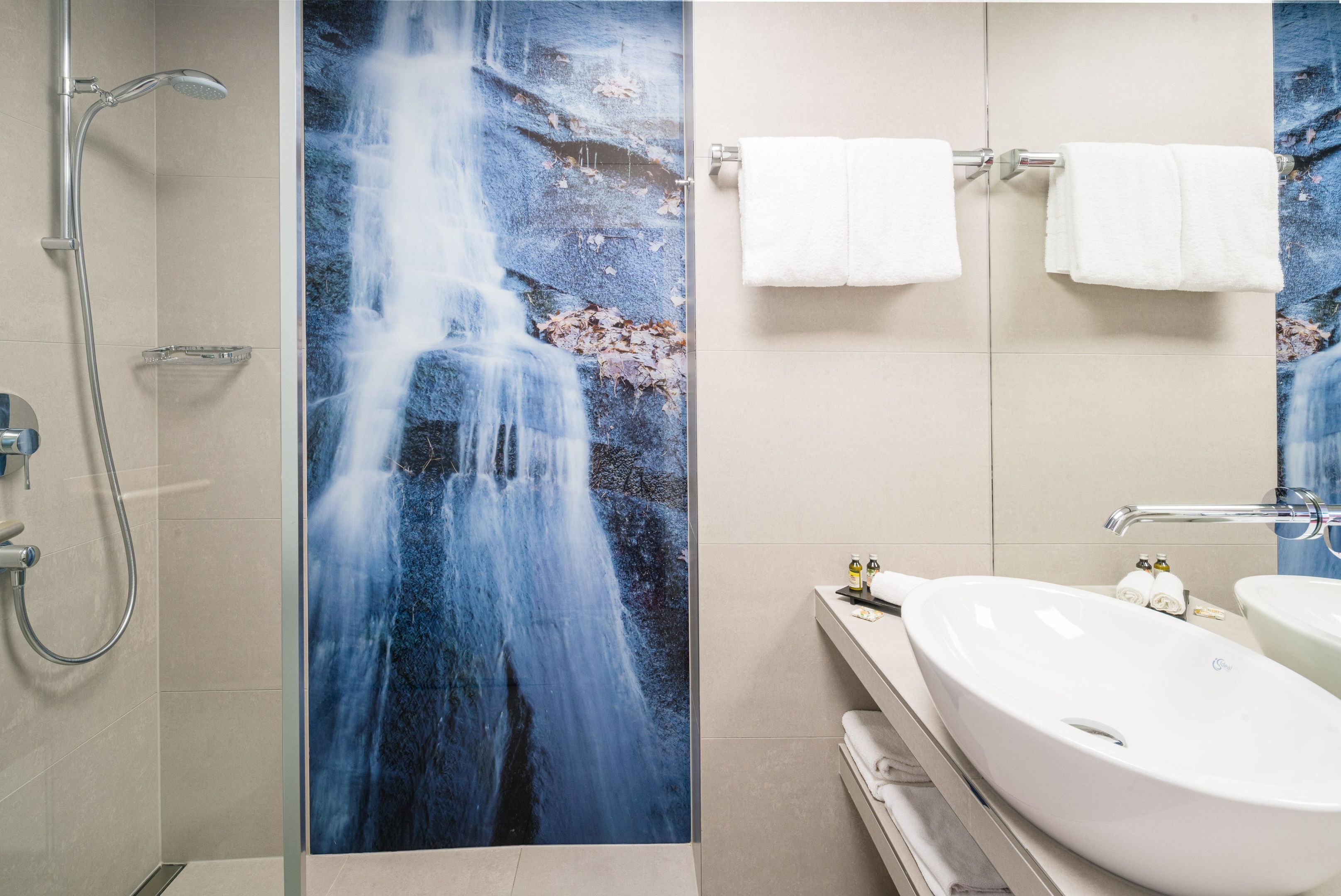 Baño con un mural grande de cascada, ducha y lavamanos con toallas.
