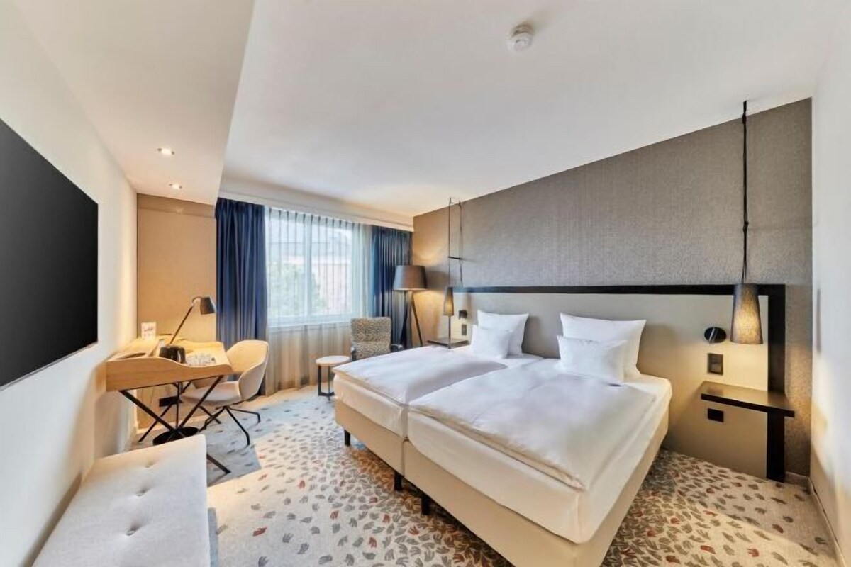 Habitación de hotel con dos camas, un escritorio, una silla, un televisor y una ventana con cortinas.