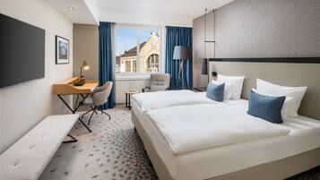 Una camera d'albergo con un letto grande, una scrivania, una sedia, una panca e vista su un edificio dalla finestra.
