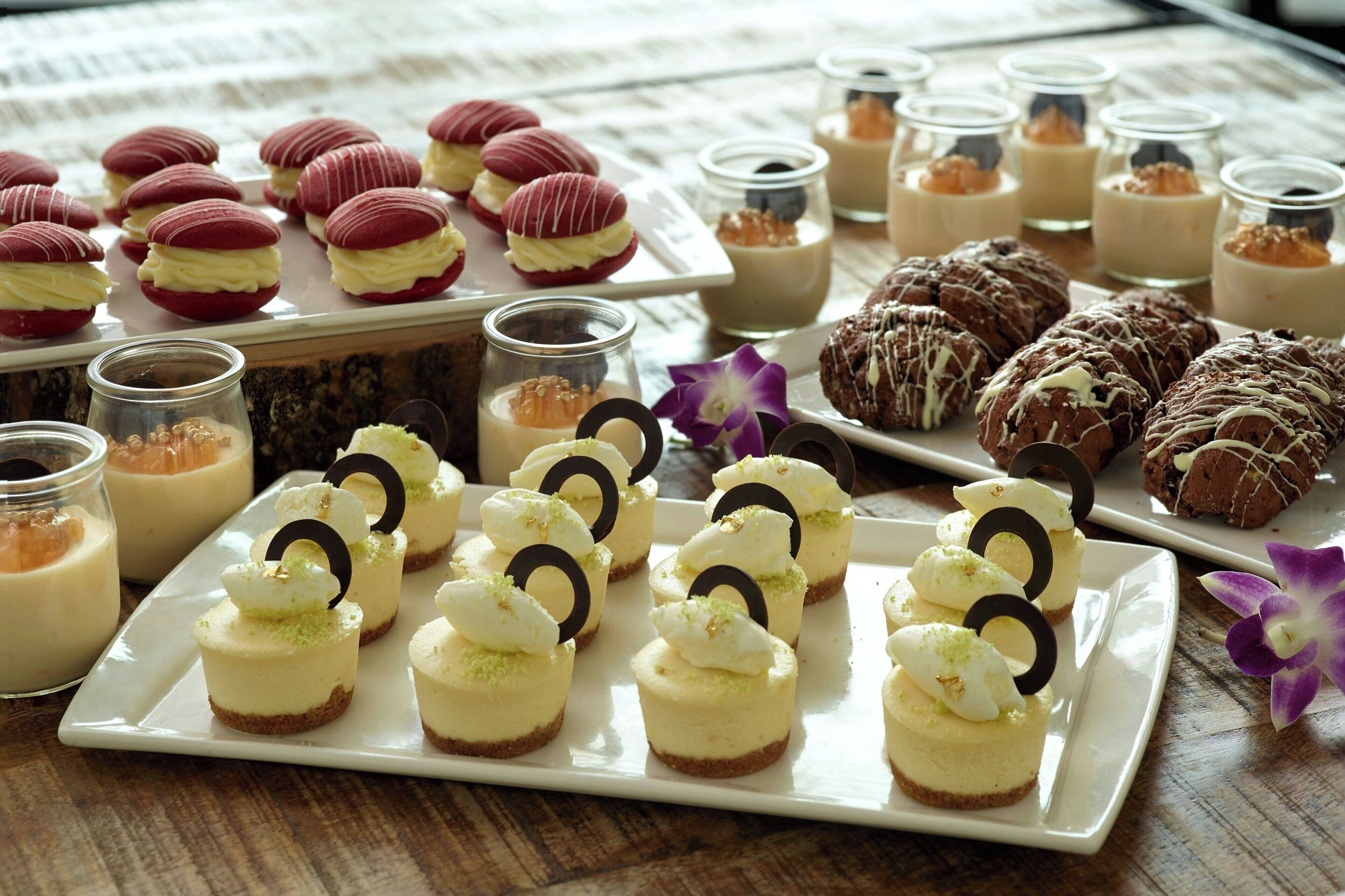 A variety of desserts on a table, including macarons, cupcakes, and small cheesecakes.