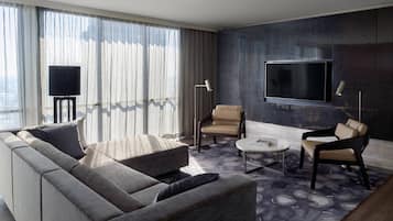 A modern living room with a sofa, two armchairs, a coffee table, a flat-screen TV mounted on the wall, and a floor lamp.