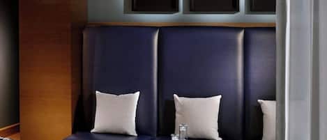 A modern lounge area with a dark blue sofa, two armchairs, and a round wooden coffee table. There are three framed pictures on the wall above the sofa.