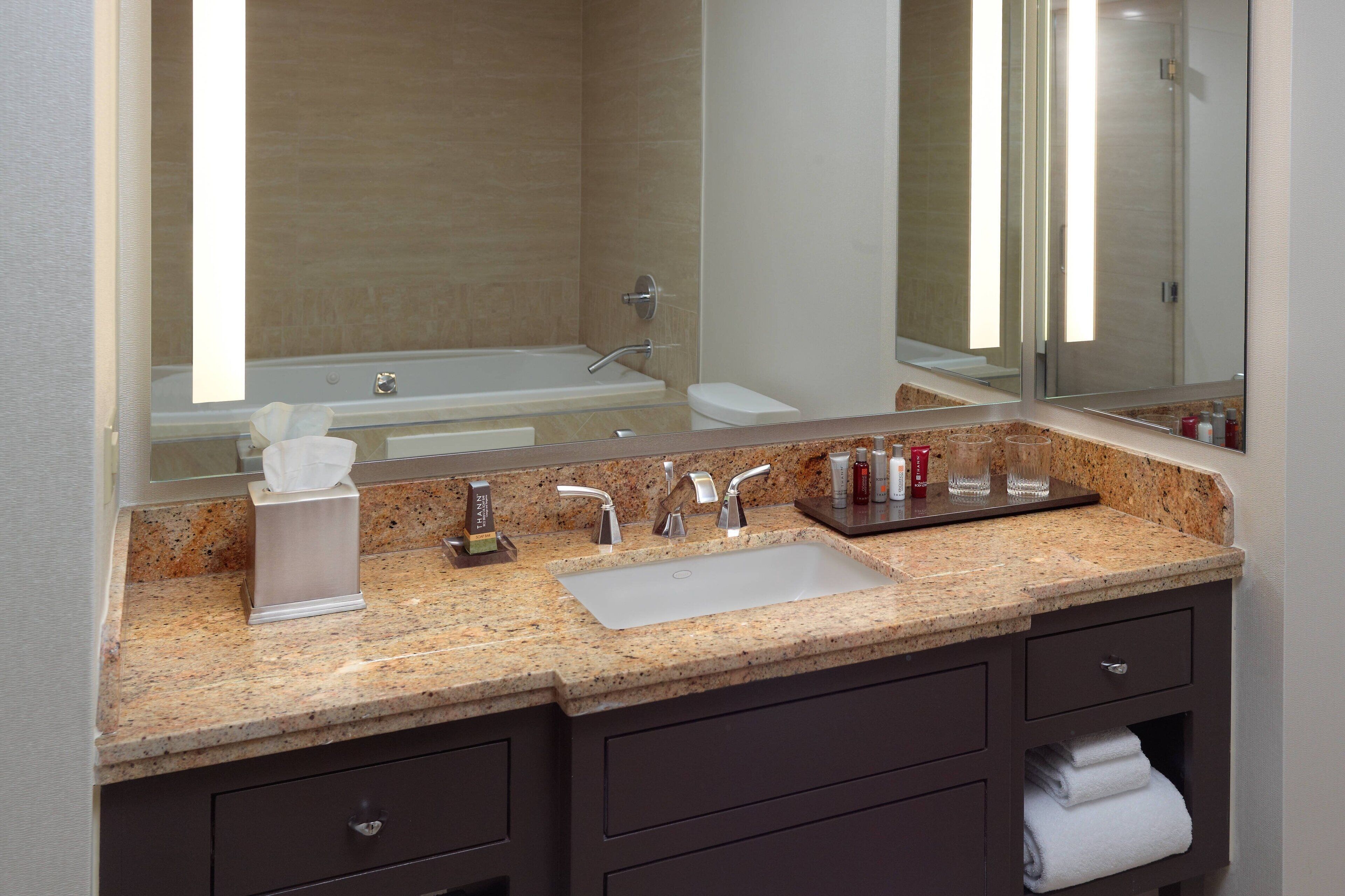 A modern bathroom with a granite countertop, a sink, a mirror, and a bathtub.