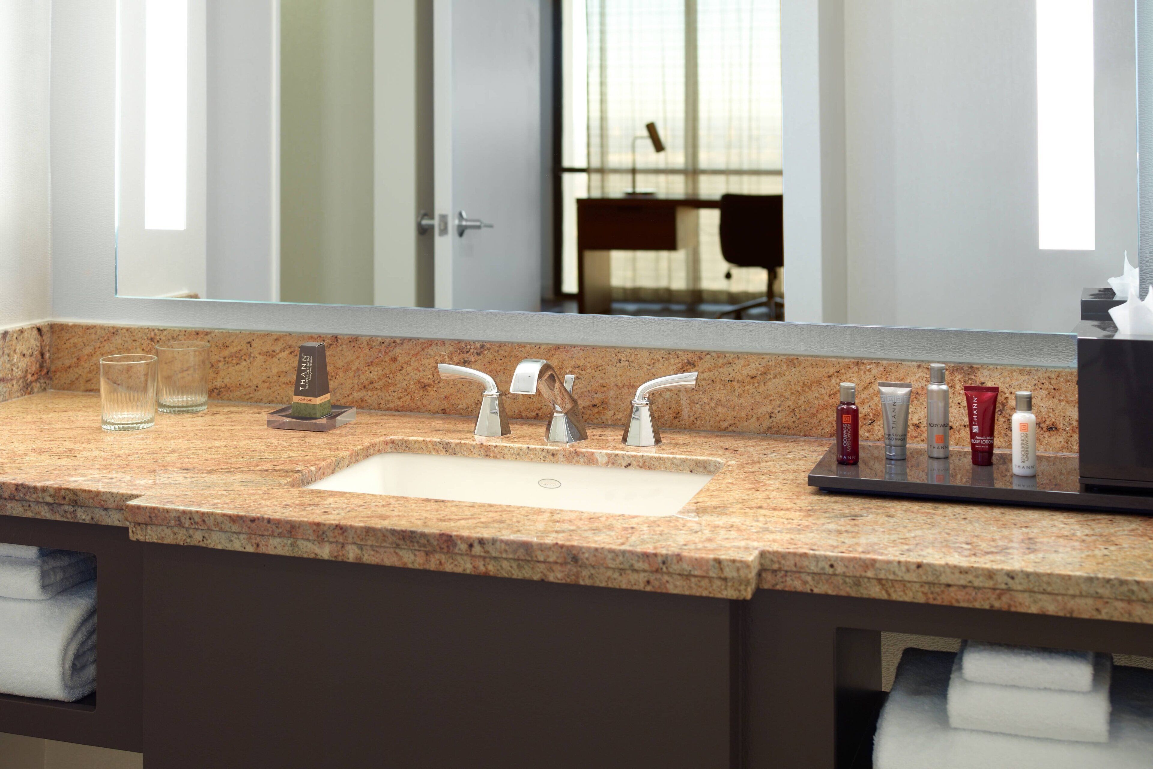A bathroom with a granite countertop, a sink with two faucets, and a mirror above it.