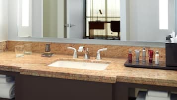 A bathroom with a granite countertop, a sink with two faucets, and a mirror above it.