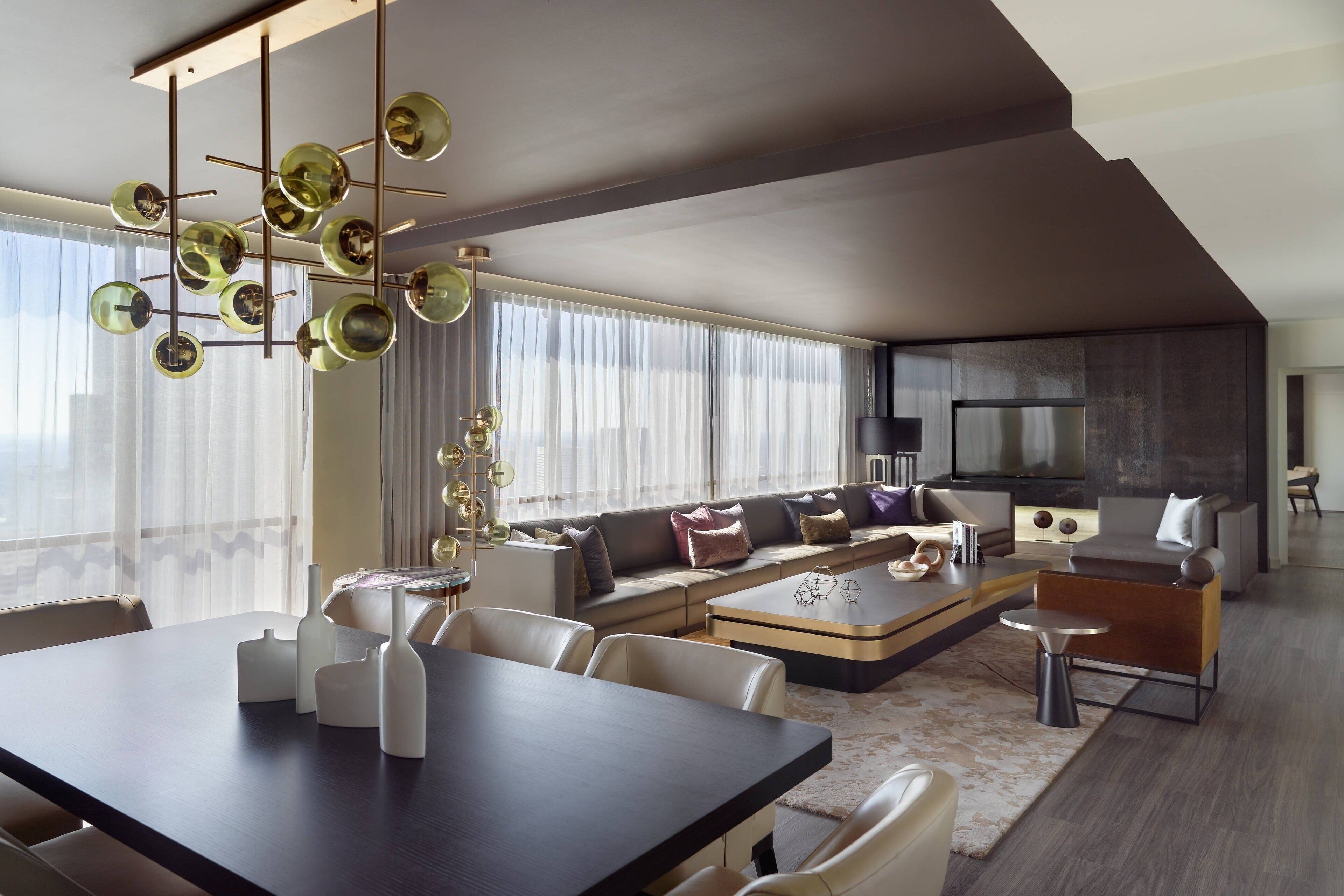 A modern living room with a dark wood dining table, white chairs, a sofa with cushions, and a large flat-screen TV.