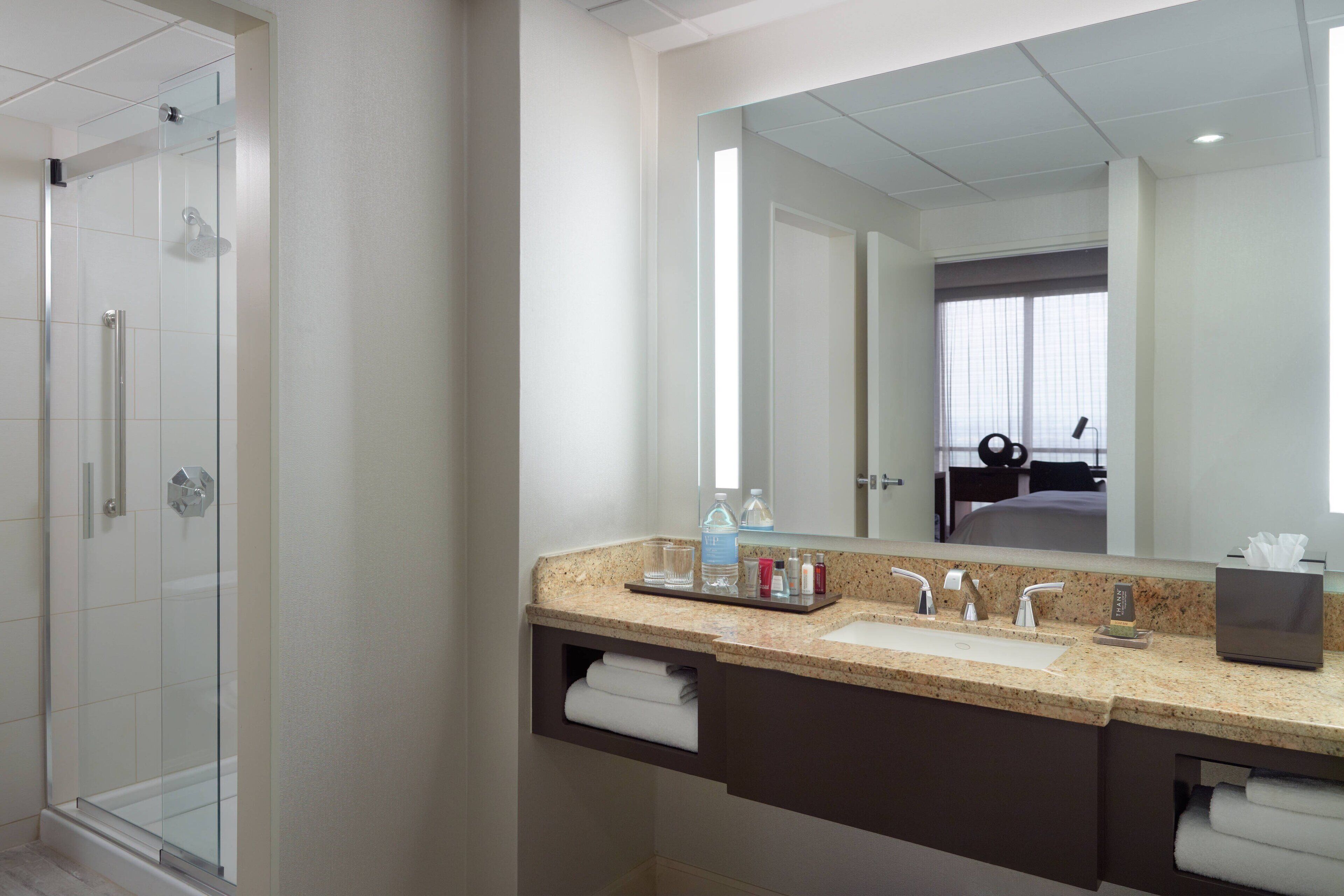 A modern bathroom with a glass-enclosed shower, a large mirror, and a granite countertop with a sink and vanity.