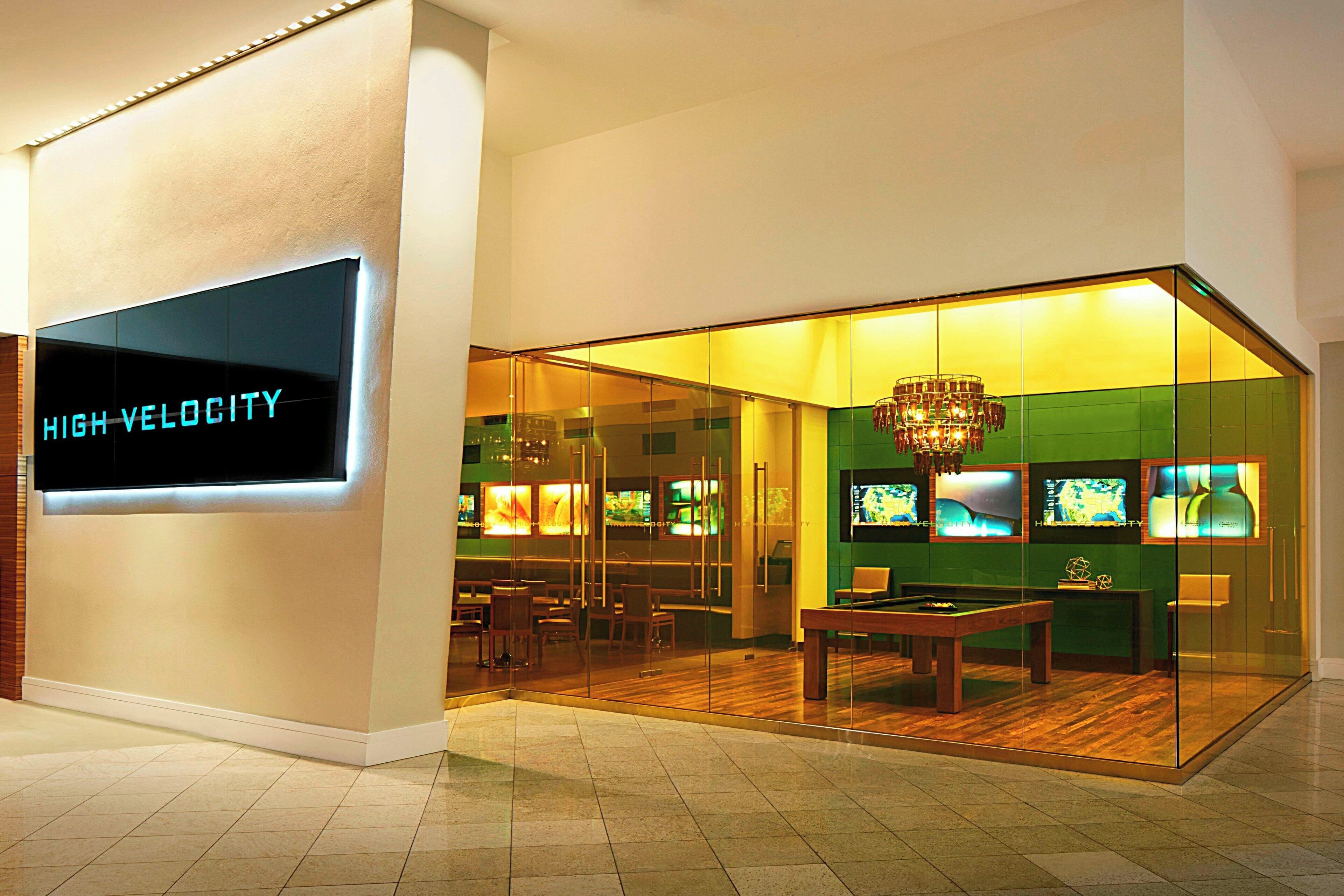 A modern interior with a billiards table, a chandelier, and a sign reading "HIGH VELOCITY".