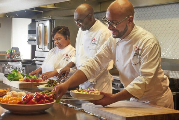 Chefs preparing food in a professional kitchen with stainless steel appliances and a clean, organized layout.