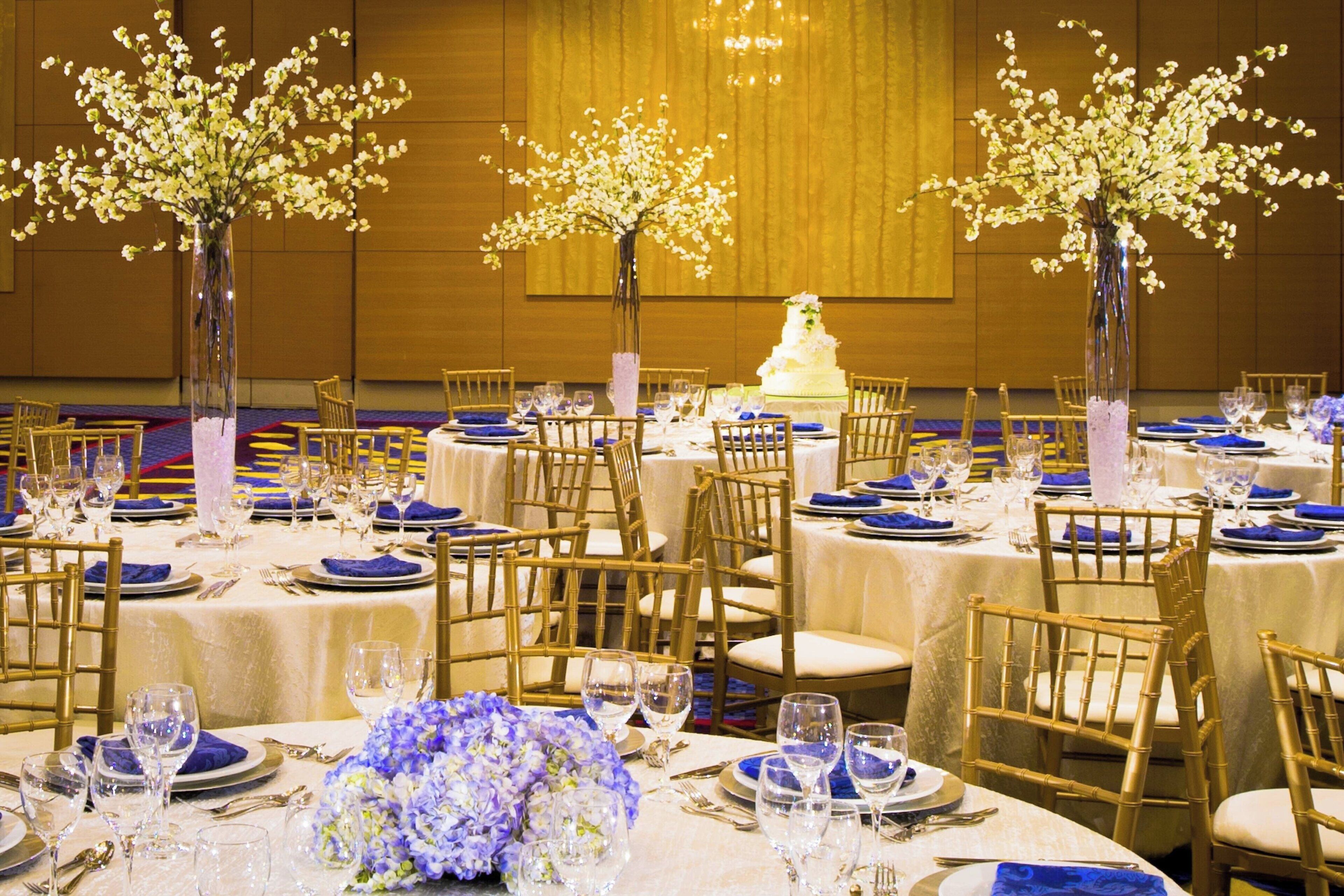 A banquet hall with round tables set for a formal event, featuring floral centerpieces and blue tablecloths.