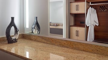 A bathroom with a granite countertop, a mirror, a white robe hanging on a rack, and a wooden cabinet.
