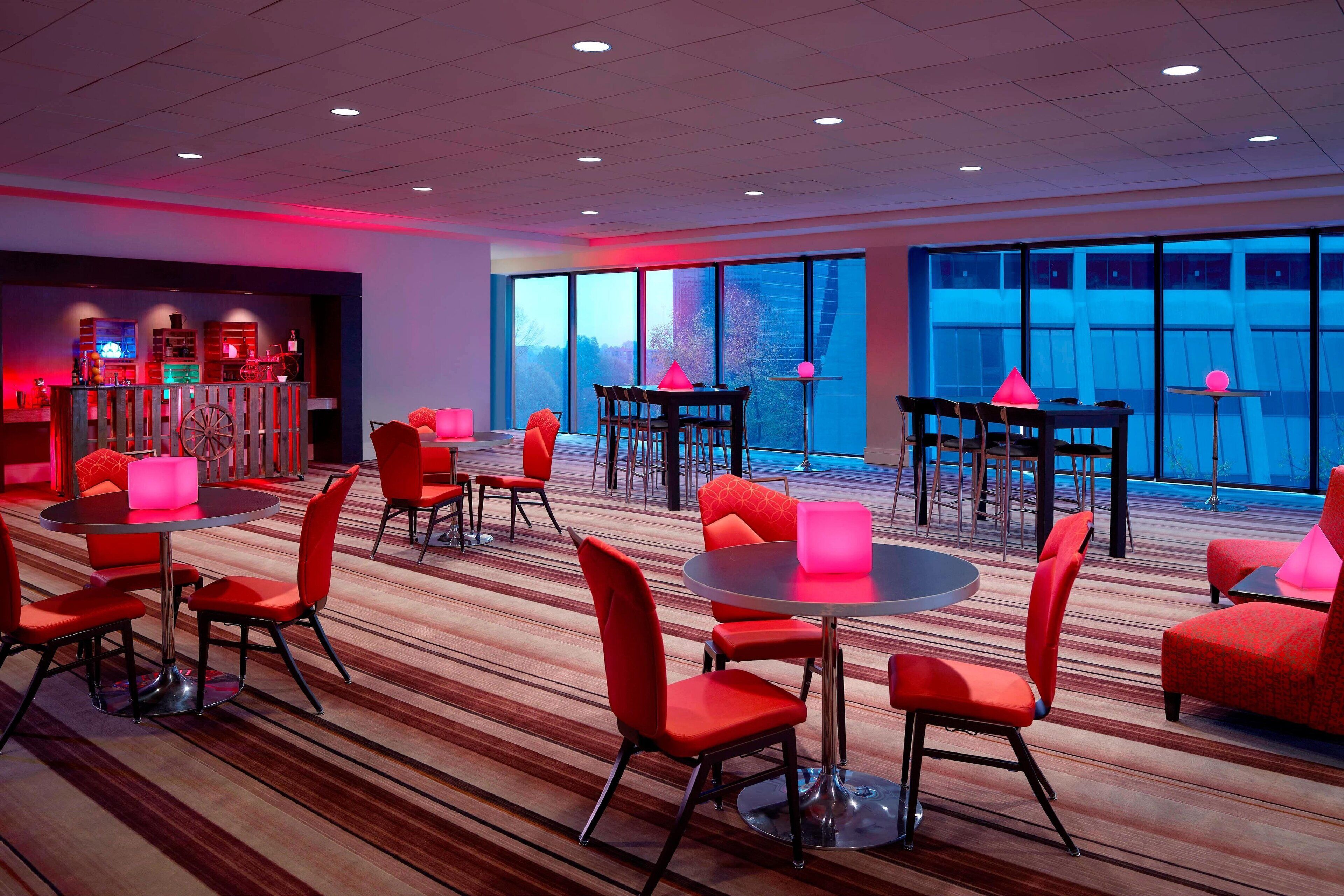 A modern hotel lobby with multiple seating areas, large windows, and a bar area.