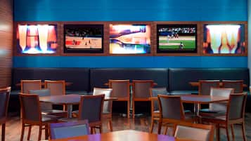 Ein Restaurant mit mehreren Bildschirmen, die Sportereignisse zeigen, Holztischen und -stühlen sowie einer dunkelblauen Wand.