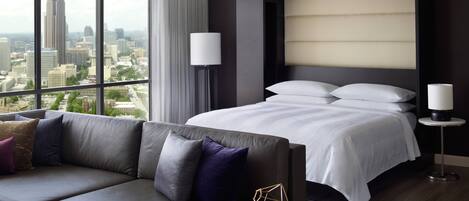 Una habitación de hotel moderna con una cama grande, un sofá y vistas a un paisaje urbano.