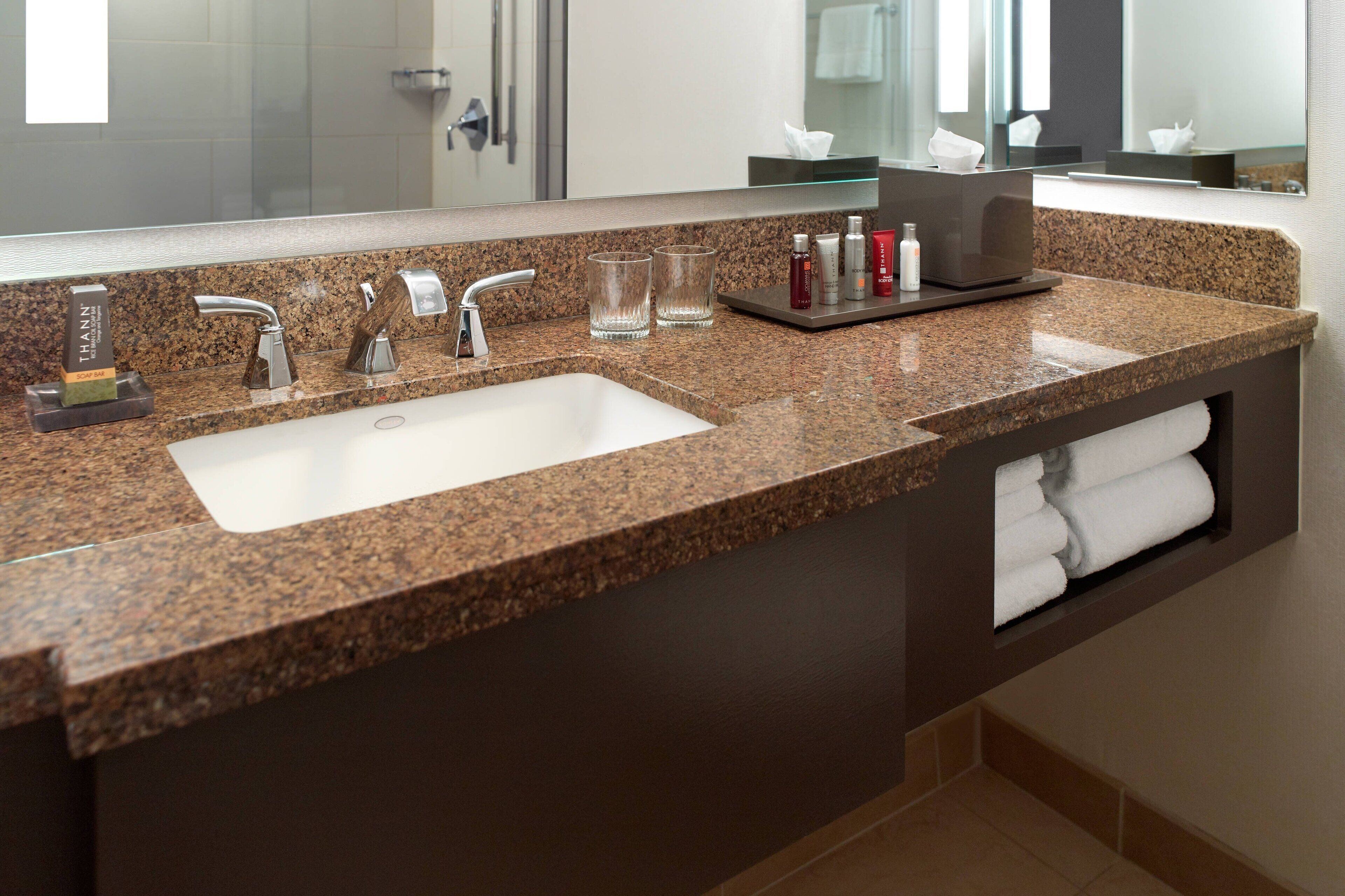 A bathroom with a granite countertop, two sinks, a mirror, and a towel rack.