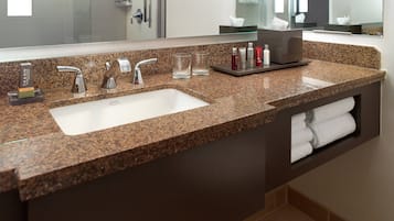 A bathroom with a granite countertop, two sinks, a mirror, and a towel rack.
