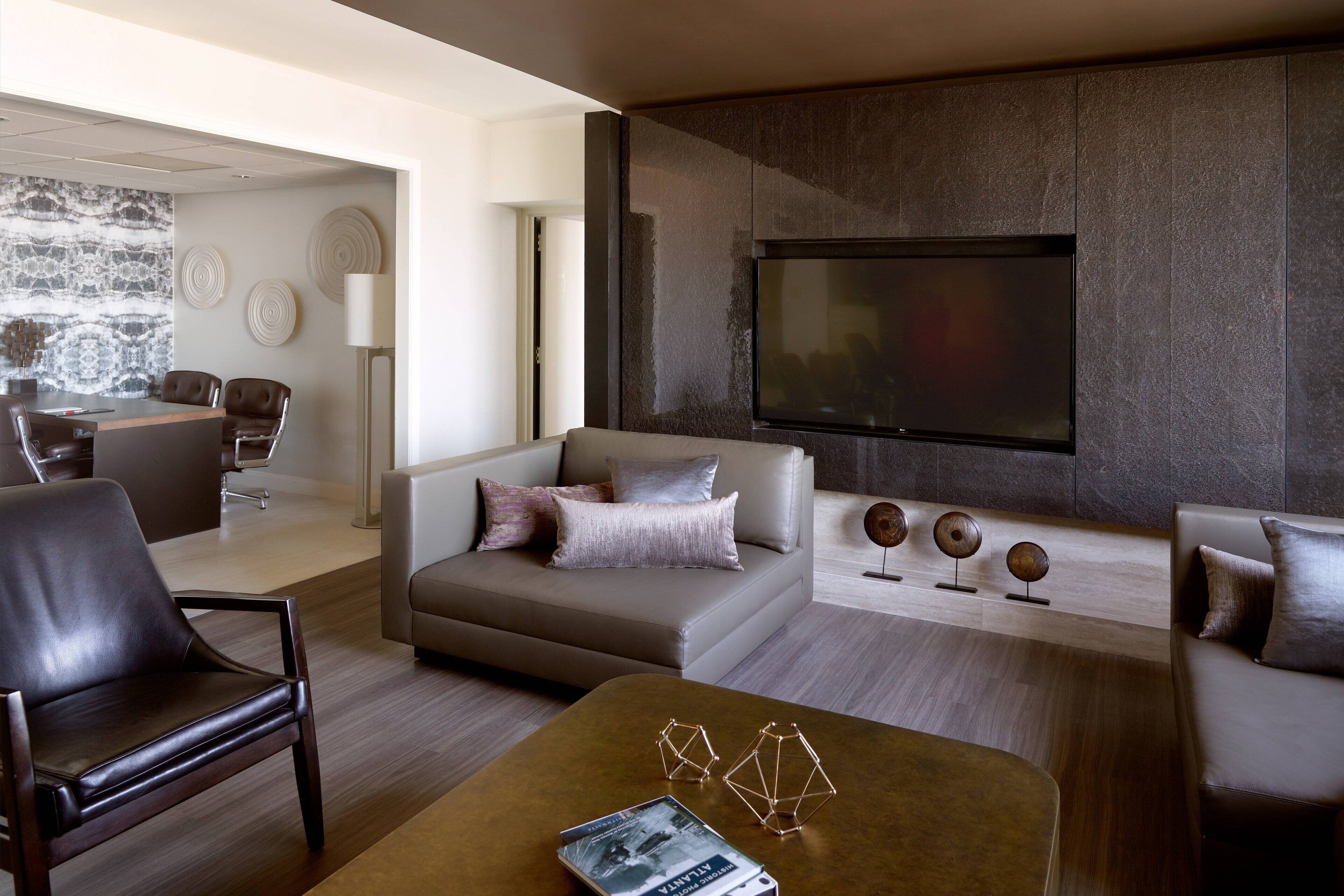 A modern living room with a sofa, armchairs, a coffee table, and a flat-screen TV mounted on a textured wall.