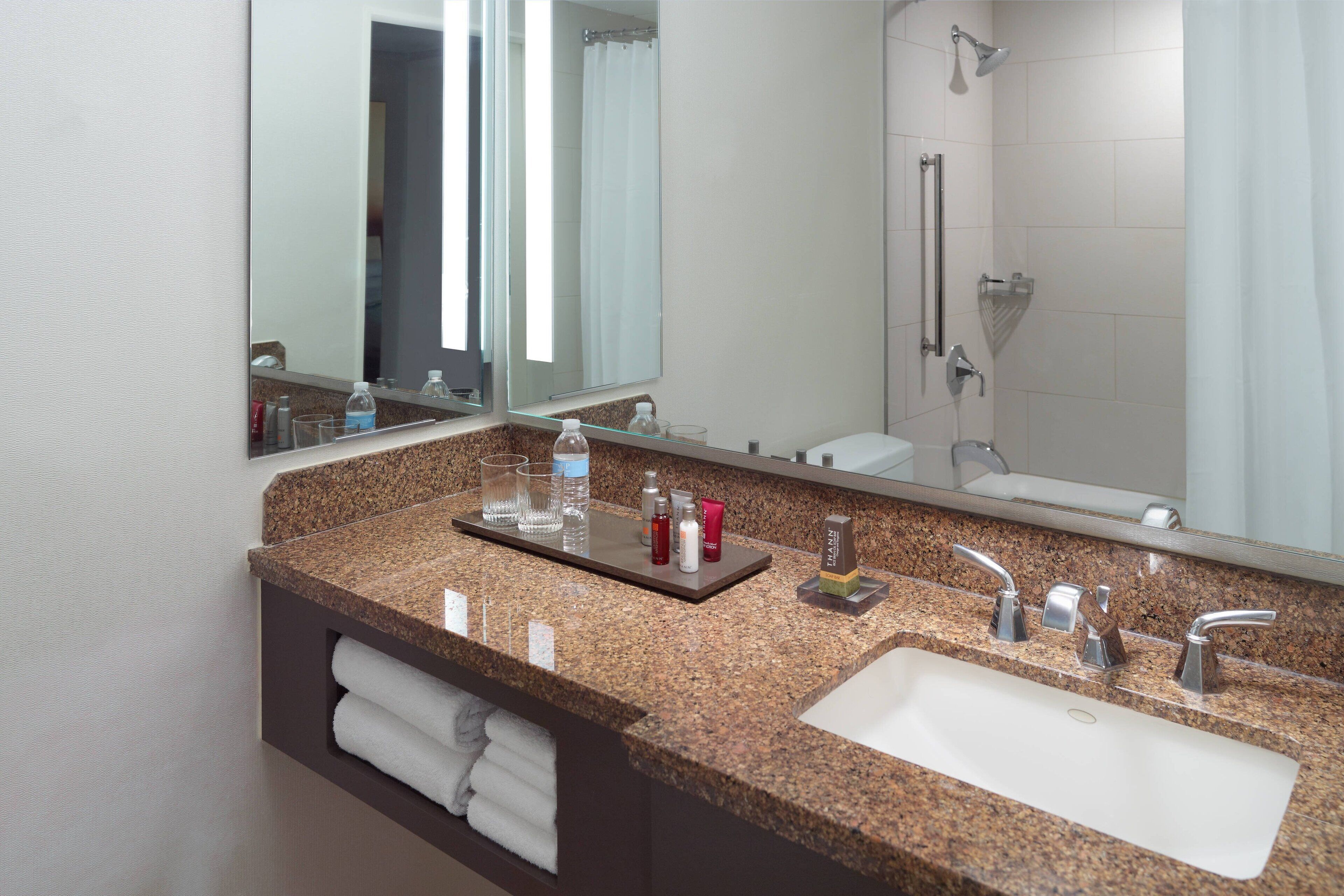 Een badkamer met een granieten aanrechtblad, een wastafel, een spiegel en een douche.