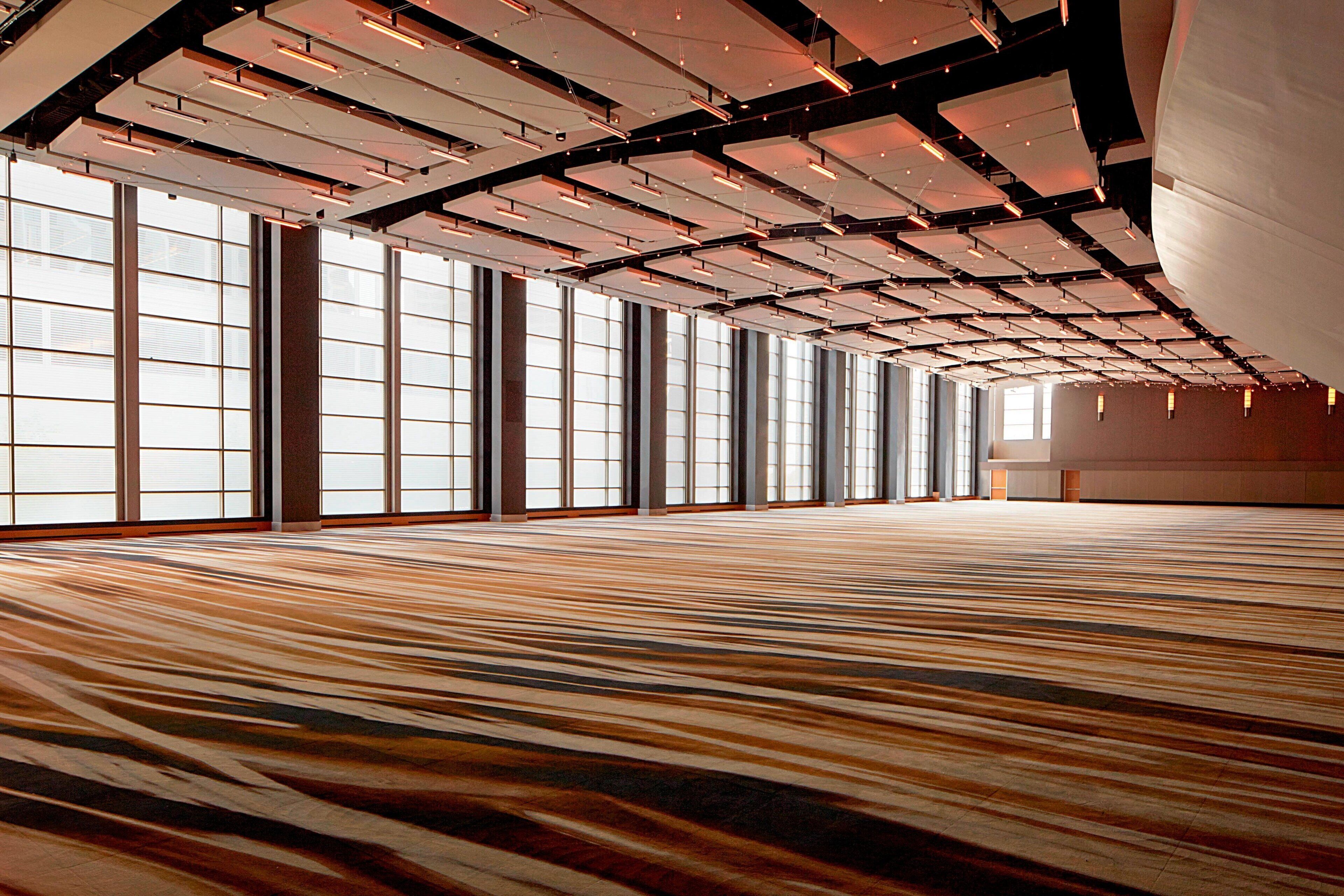 Ein geräumiger Saal mit Teppichmuster, großen Fenstern und einer hohen Decke mit freiliegenden Balken.