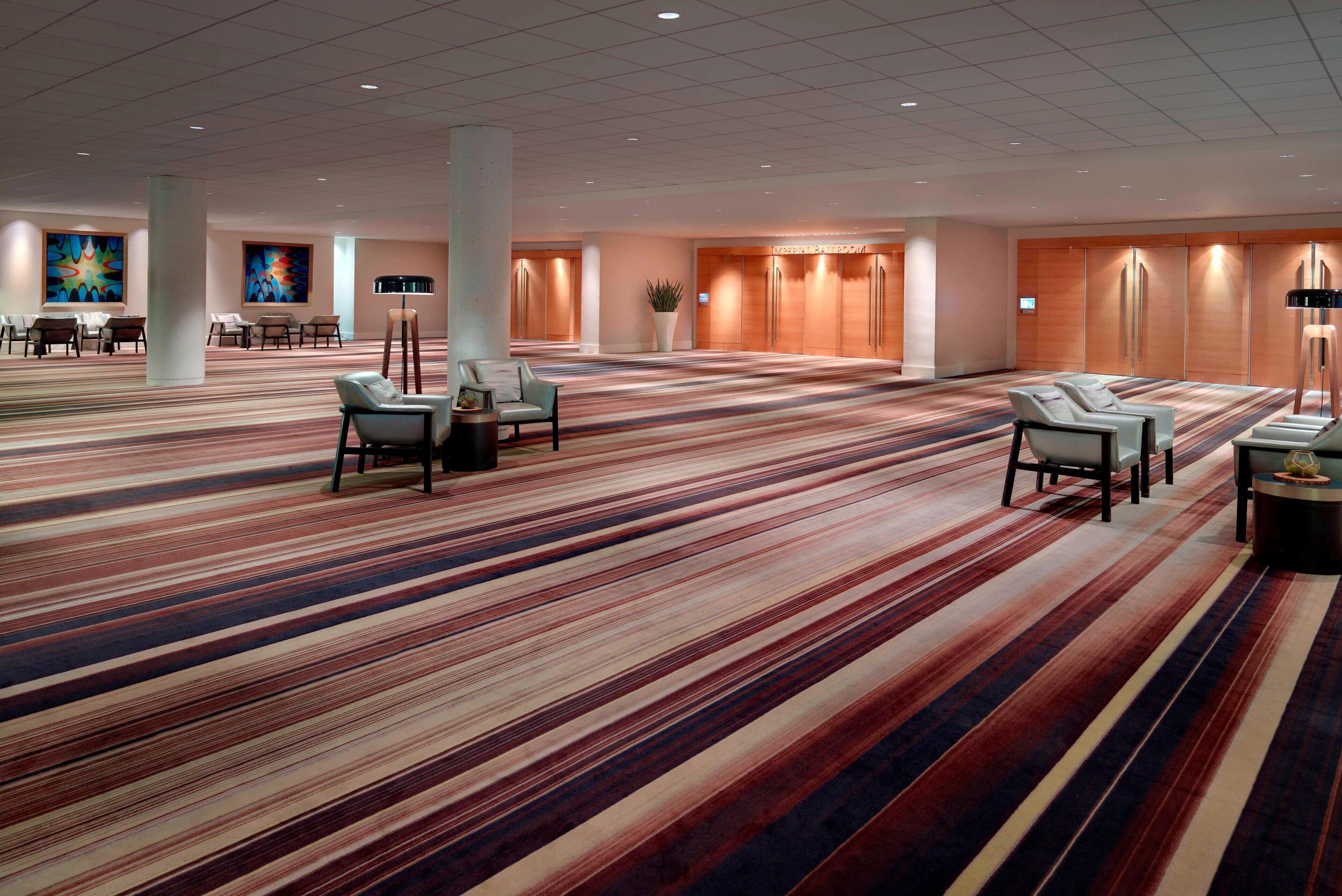 A spacious hotel lobby with striped carpeting, multiple seating areas, and a large plant.