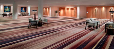 A spacious hotel lobby with striped carpeting, multiple seating areas, and a large plant.