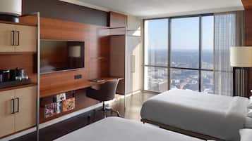 A hotel room with a large window, a desk, a bed, and a TV.