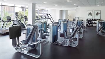 A gym with various exercise machines, large windows, and a wall with framed pictures.