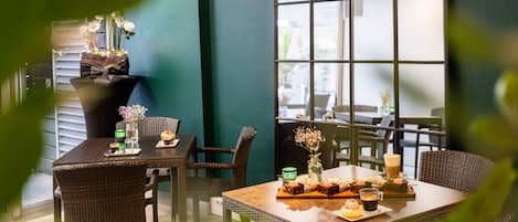 Un restaurante con mobiliario de mimbre, un ventanal grande y una mesa dispuesta con postres y bebidas.