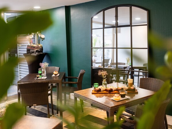 Un restaurante con mobiliario de mimbre, un ventanal grande y una mesa dispuesta con postres y bebidas.