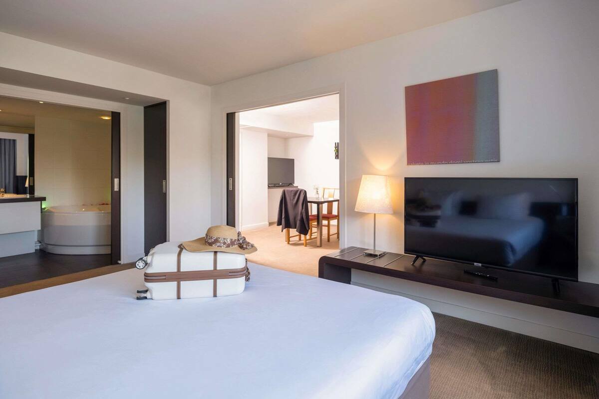 A hotel room with a bed, a television, a desk, a lamp, and a suitcase.
