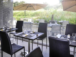 Un espacio de comedor al aire libre con mesas, sillas, posavasos numerados y copas de vino.