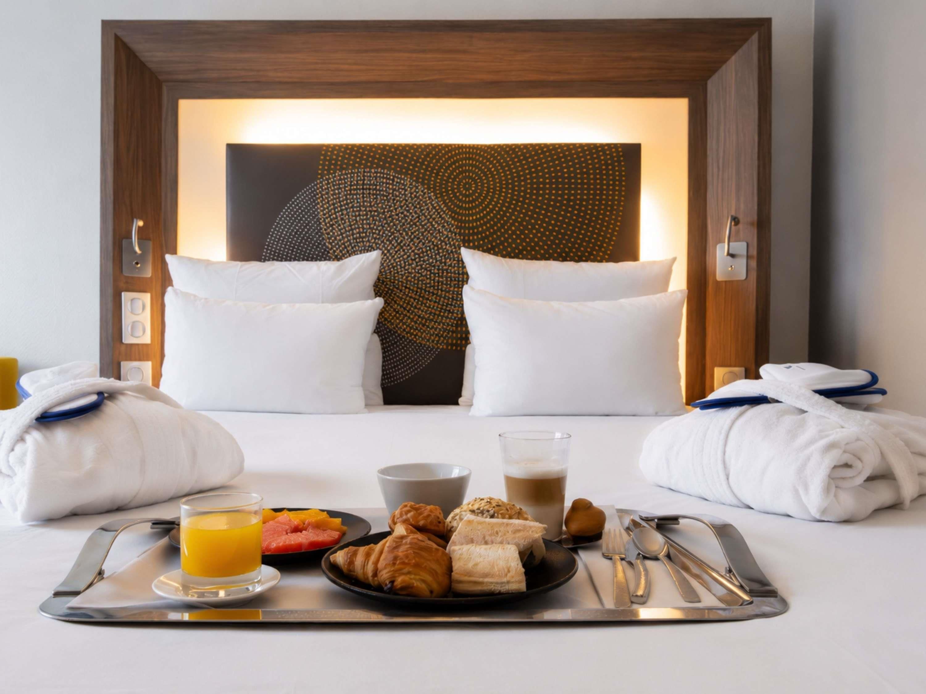 A hotel room with a bed, pillows, a tray with breakfast, and a wall art piece.