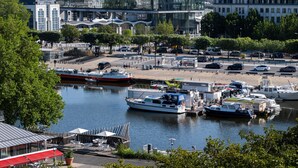 Un port de plaisance avec des bateaux amarrés, un bâtiment moderne à la façade vitrée et, au loin, le clocher d’une église historique.