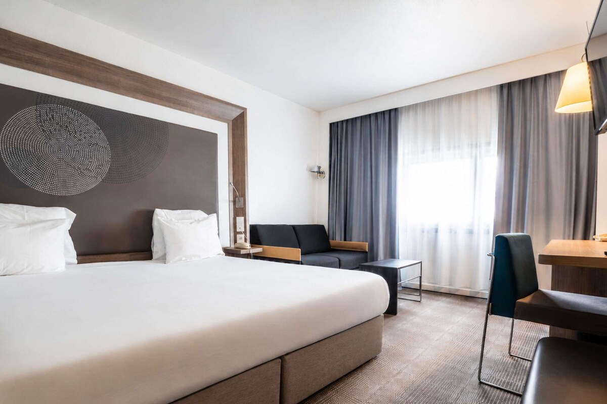 Una habitación de hotel moderna con una cama grande, un escritorio, una silla y un sofá.