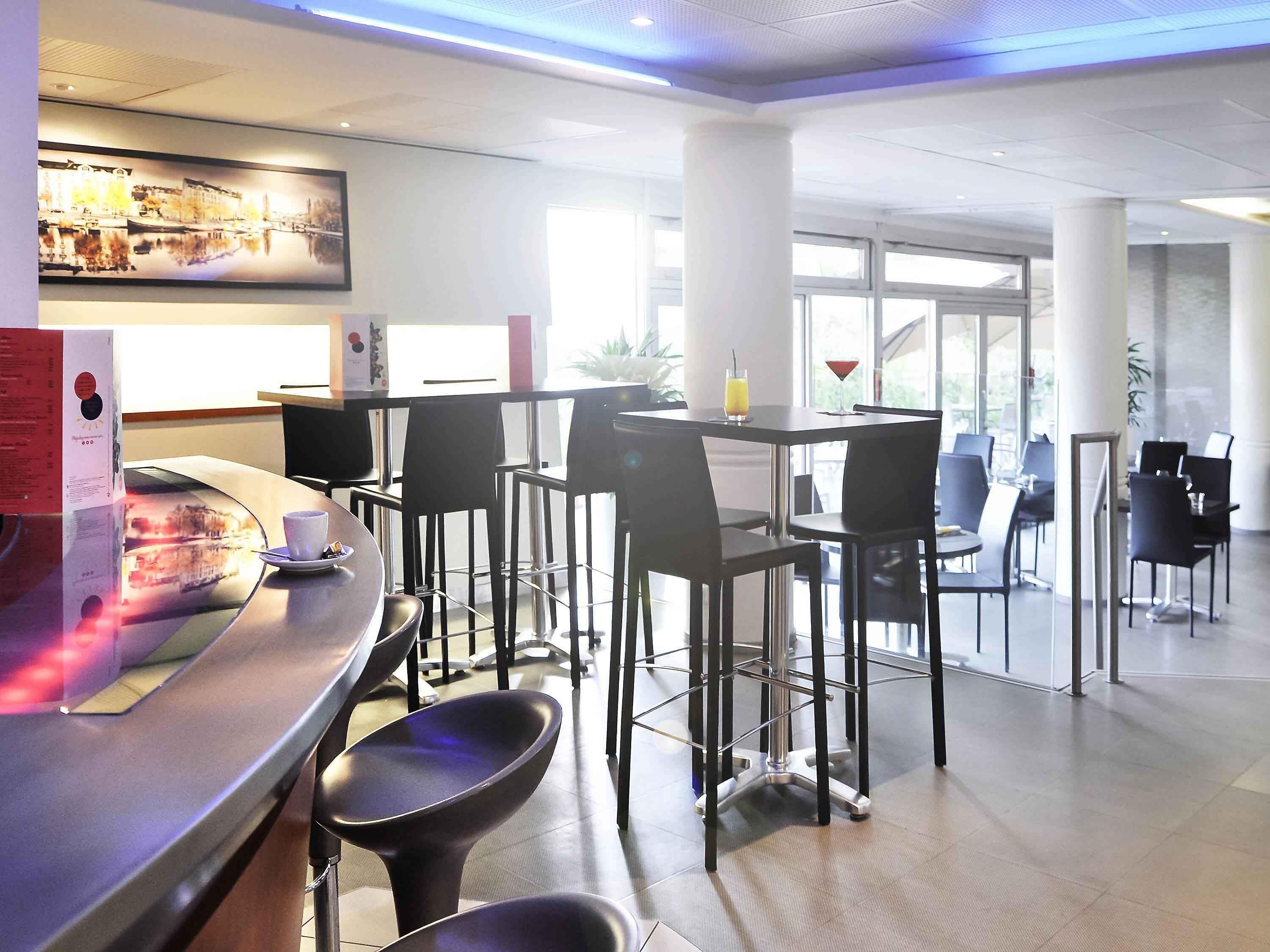 Un hall d’hôtel moderne doté d’un bar, de coins salon et d’une grande fenêtre laissant entrer la lumière naturelle.