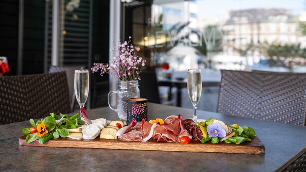 Une table avec une planche de charcuterie, un vase rempli de fleurs et deux coupes de champagne.
