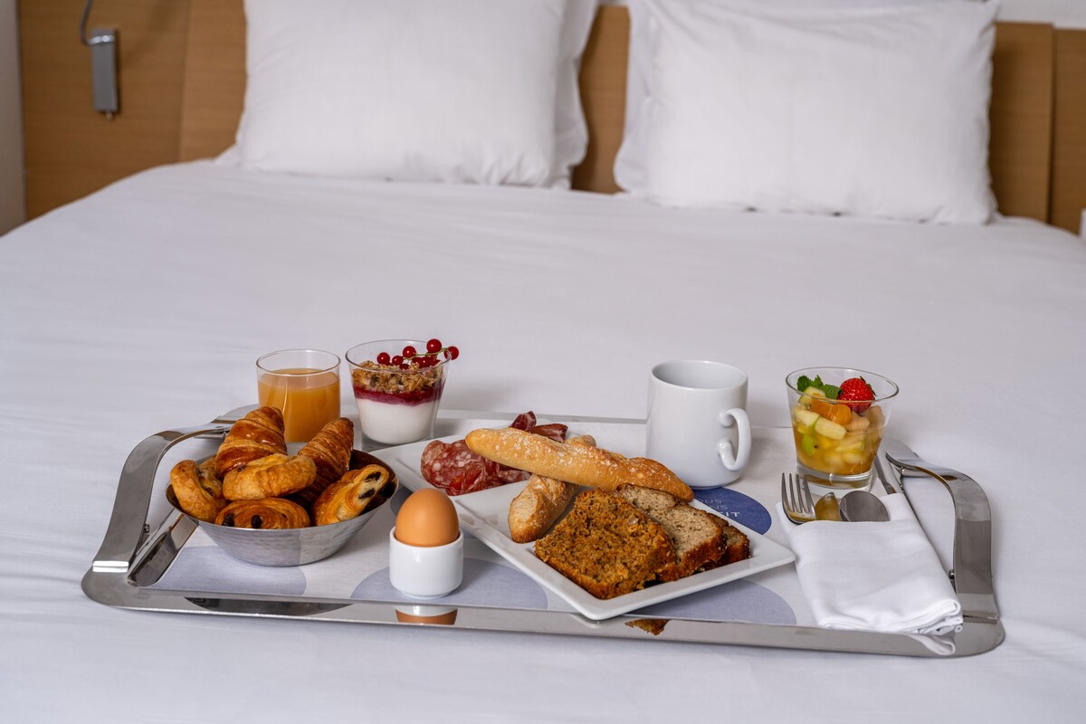 Een ontbijttafel met croissants, brood, eieren en fruit op een hotelbed.
