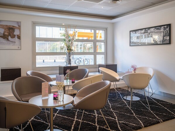 A modern hotel room with a large window, a black and white patterned rug, and several chairs around a small table.