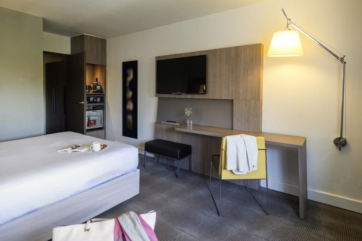 Een hotelkamer met een bed, een bureau, een televisie, een lamp en een minibar.